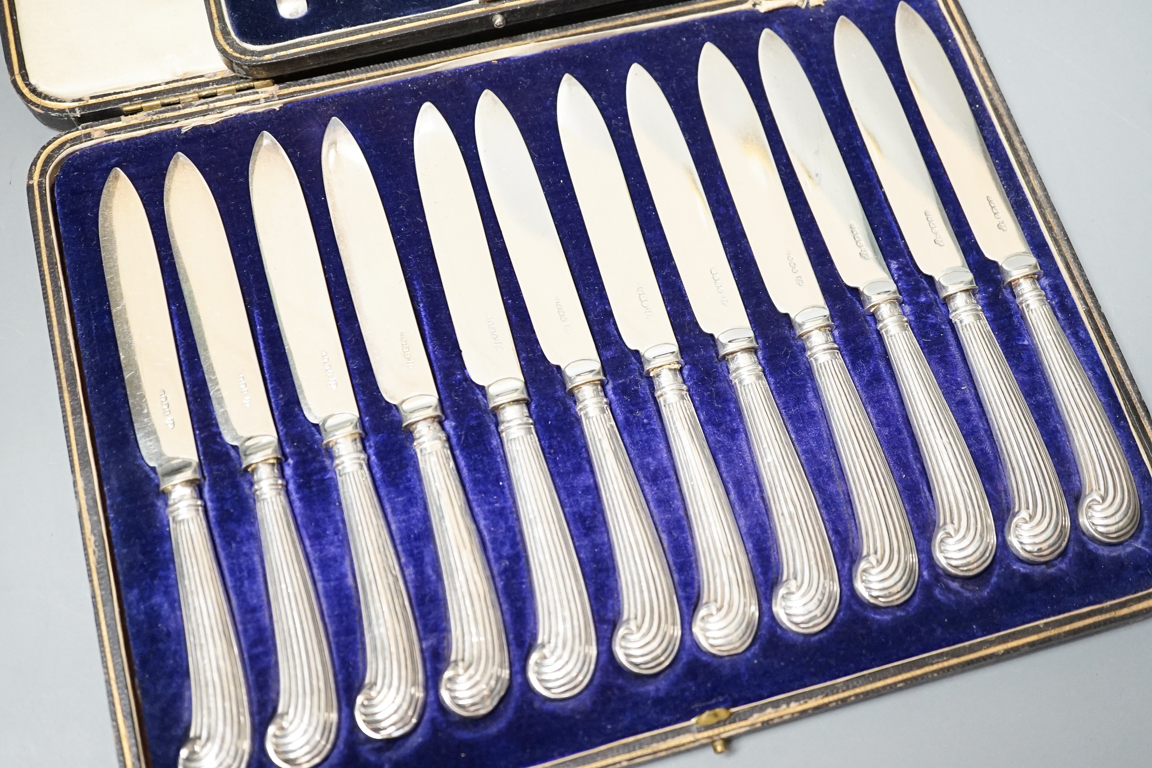 A cased set of twelve reeded silver pistol handled steel dessert knives and a cased set of six silver teaspoons.